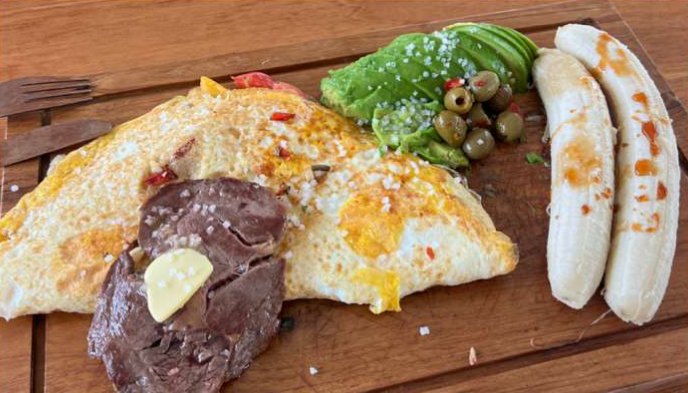 Tortilla con entrecot, aguacate, aceitunas y plátano sobre tabla de madera